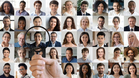 Male hr manager holding magnifying glass head hunting choosing finding new unique talent indian female candidate recruit among multiethnic professional people faces collage. Human resources concept.